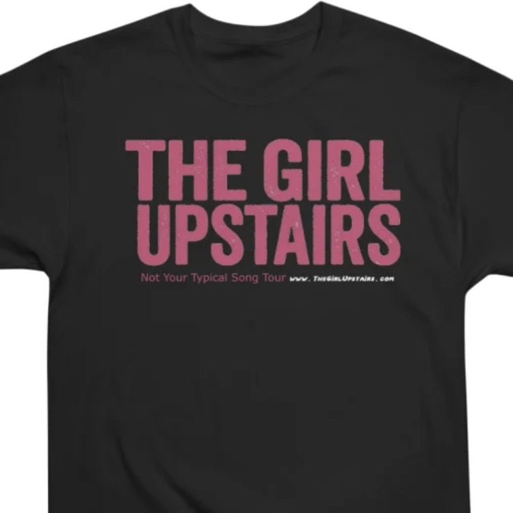 Black T-shirt featuring pink “THE GIRL UPSTAIRS” text and small tour slogan beneath.